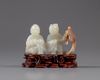 A pale jade carving of two boys with a wooden stand