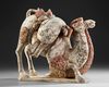 A PAINTED TERRACOTTA KNEELING CAMEL WITH SADDLE PACK, CHINA, TANG DYNASTY (618-906 AD)