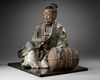 A JAPANESE SEATED LEGENDARY FIGURE WITH HAY BALE, 18TH CENTURY