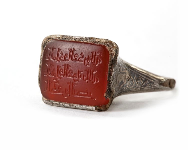 AN ISLAMIC NIELLOED  SILVER RING SET WITH AN INSCRIBED CORNELIAN IN A SQUARE BEZEL, MOSUL AREA, 8TH-9TH CENTURY