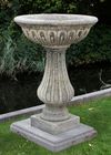 A CARVED LIMESTONE PLANTER ON A PLINTH