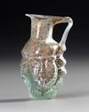 A SMALL GLASS EWER WITH MASK-LIKE RELIEF
