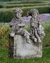 A PAIR OF COMPOSTION STONE SITTING PUTTI’S, 20TH CENTURY (NO BASE)