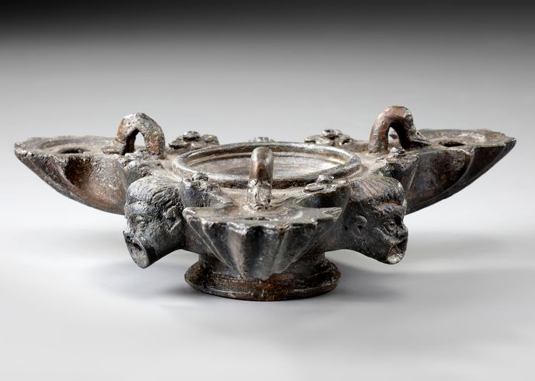 A ROMAN BRONZE THREE-NOZZLED OIL LAMP WITH THEATRE MASK AND ROSETTES AS DECORATION, CIRCA 1ST-2ND CENTURY A.D.
