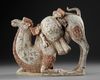 A PAINTED TERRACOTTA KNEELING CAMEL WITH SADDLE PACK, CHINA, TANG DYNASTY (618-906 AD)